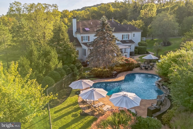 outdoor pool featuring fence, a patio area, outdoor dining space, a yard, and a forest view