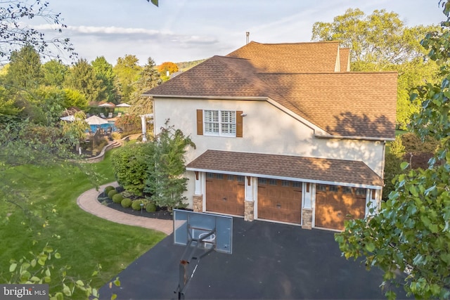exterior space featuring a shingled roof, stone siding, aphalt driveway, stucco siding, and a lawn