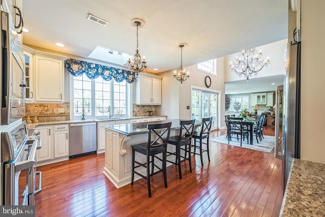 kitchen featuring an inviting chandelier, a sink, wood-type flooring, stainless steel dishwasher, and visible vents