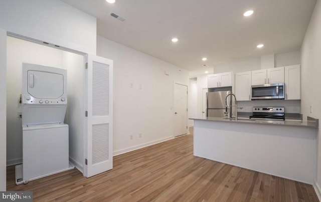 727 N 39th St, Philadelphia, PA 19104 - kitchen featuring appliances with stainless steel finishes, white cabinetry, stacked washing maching and dryer, recessed lighting, and light wood-style flooring