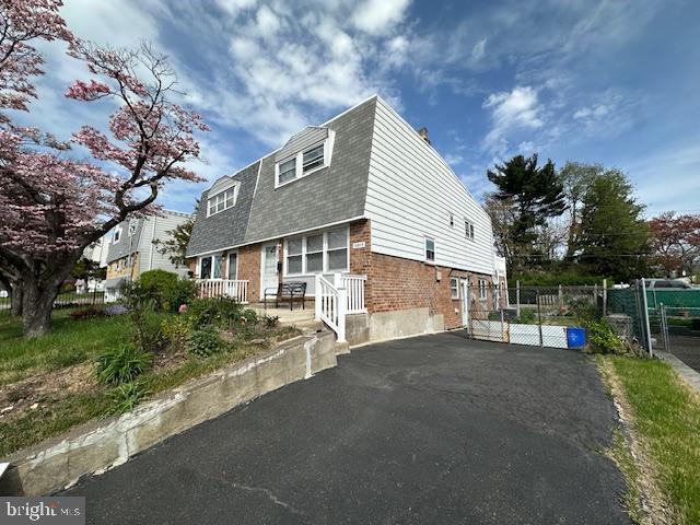view of property exterior with driveway, brick siding, fence, a gate, and roof with shingles