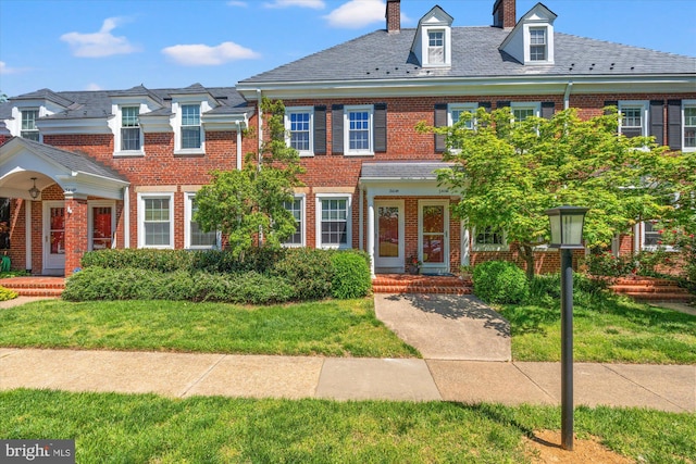 view of front of home featuring brick siding, a high end roof, a chimney, and a front yard