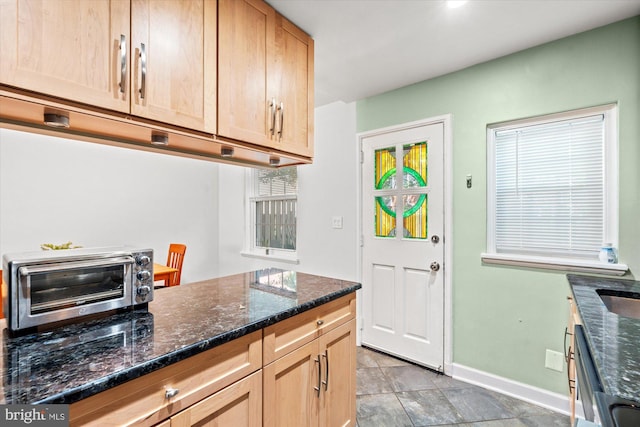 kitchen featuring light brown cabinetry, dishwasher, dark stone counters, baseboards, and a toaster