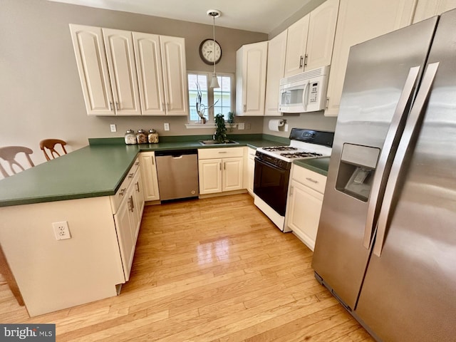 kitchen with decorative light fixtures, dark countertops, a peninsula, light wood-style floors, and stainless steel appliances