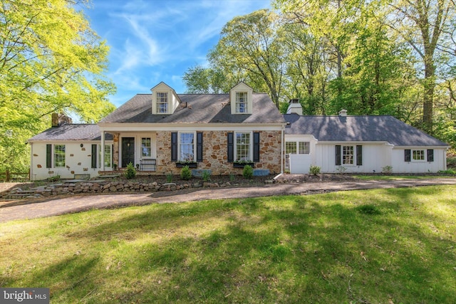cape cod home with a chimney, a front lawn, and stone siding