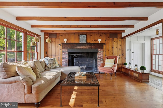 living area with a brick fireplace, beamed ceiling, a wealth of natural light, and wood finished floors