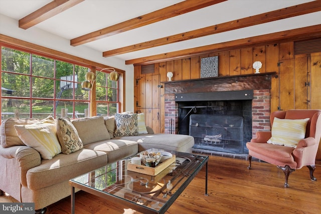 living room with wooden walls, visible vents, beam ceiling, and wood finished floors