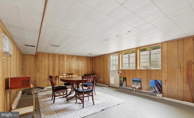 dining space with baseboards, wood walls, concrete floors, and visible vents