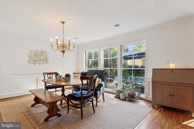 dining room with crown molding, a decorative wall, wood finished floors, a wainscoted wall, and a notable chandelier