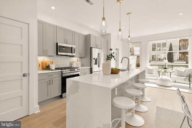 kitchen with appliances with stainless steel finishes, a sink, gray cabinets, light wood-type flooring, and backsplash