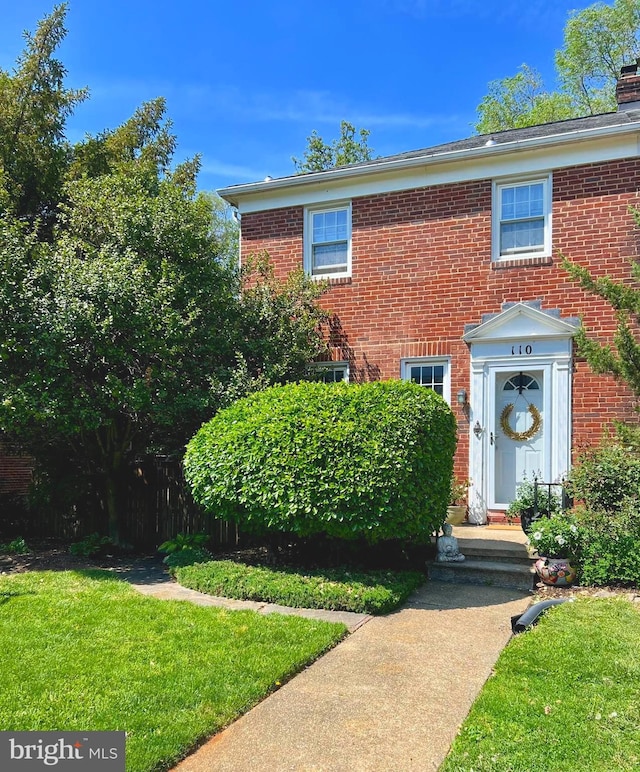 view of front of home with brick siding, a front yard, and a chimney