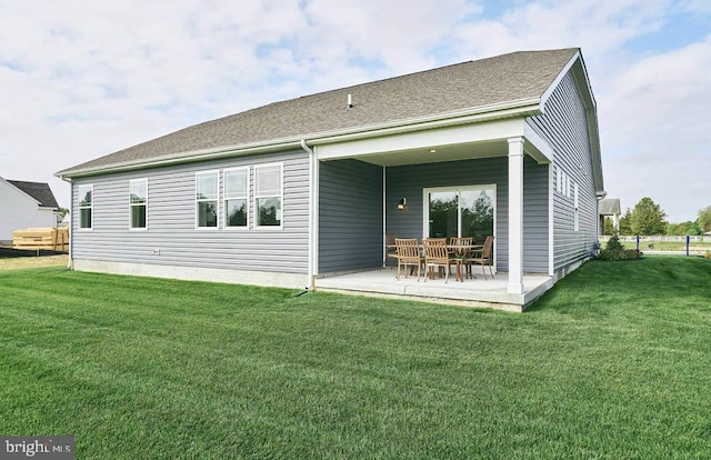 back of property featuring a lawn, a patio area, and roof with shingles