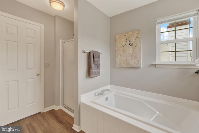 bathroom featuring wood finished floors, a shower stall, a garden tub, and baseboards