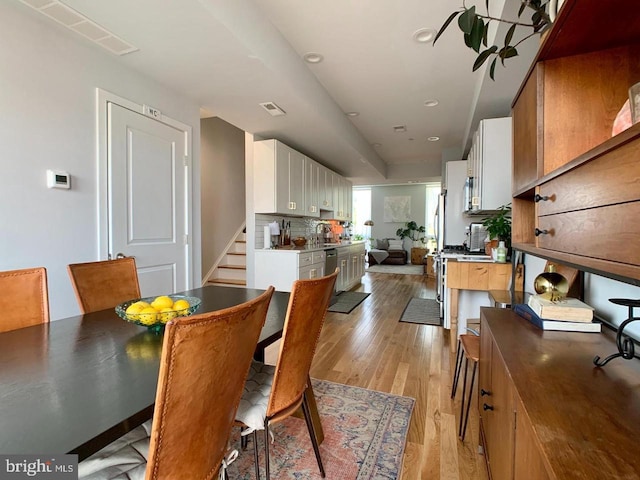 dining room with light wood-style floors, stairway, and visible vents