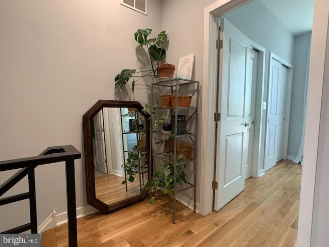 corridor with baseboards, visible vents, and wood finished floors