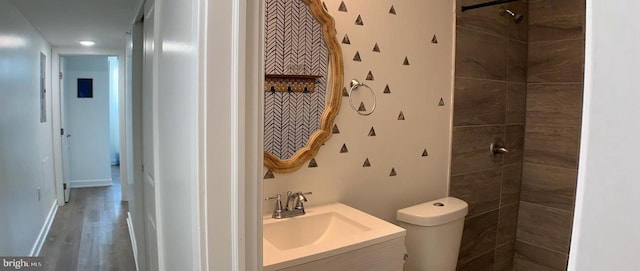 full bathroom featuring vanity, a tile shower, toilet, and wood finished floors
