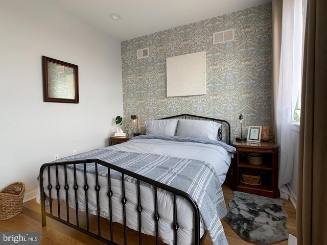 bedroom featuring baseboards, wood finished floors, visible vents, and wallpapered walls