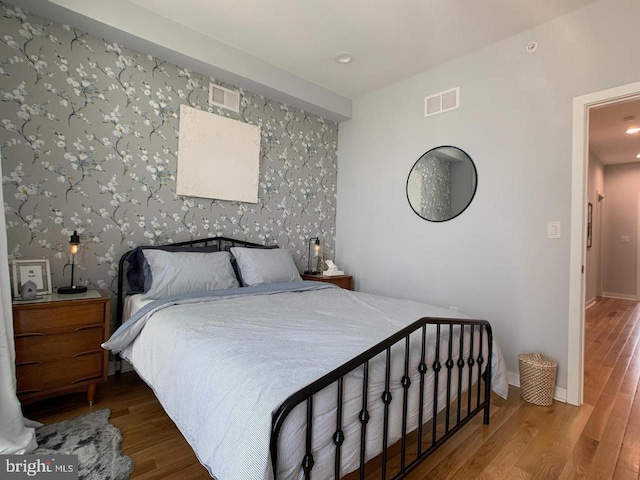 bedroom featuring baseboards, wallpapered walls, visible vents, and wood finished floors