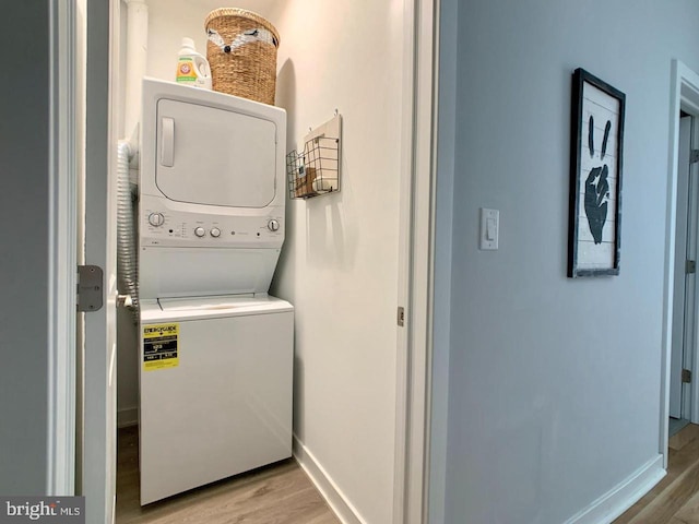 laundry room featuring baseboards, laundry area, light wood finished floors, and stacked washer and clothes dryer