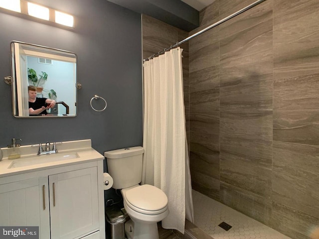 bathroom featuring vanity, a tile shower, toilet, and visible vents