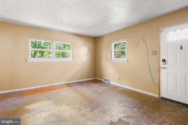 empty room with baseboards, a textured ceiling, wood finished floors, and visible vents