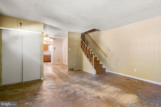 unfurnished living room featuring a textured ceiling, visible vents, baseboards, and stairway