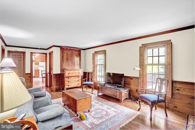living room featuring wood walls, ornamental molding, wood finished floors, and a wainscoted wall