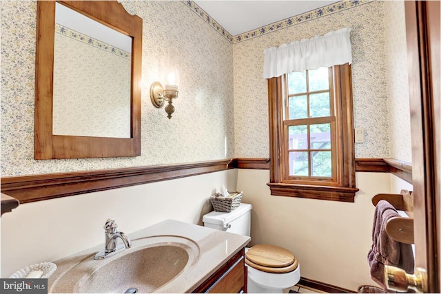 half bathroom with vanity, toilet, and wallpapered walls