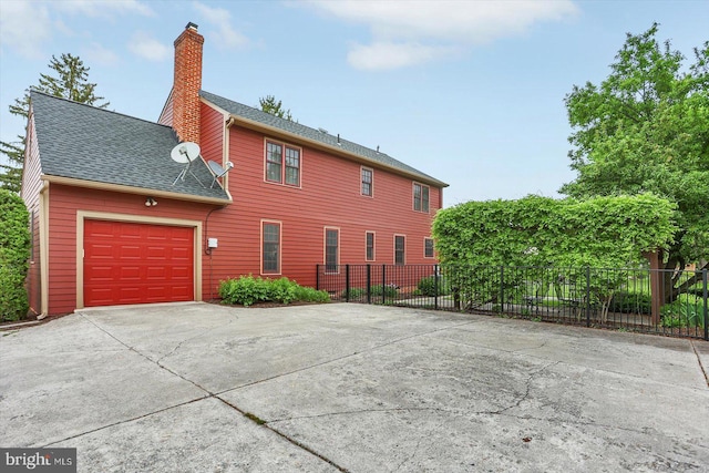 back of property with fence, roof with shingles, an attached garage, a chimney, and driveway