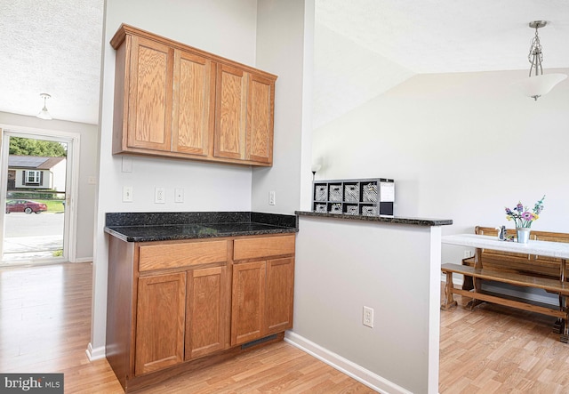 702 Rainbow Ct, Edgewood, MD 21040 - kitchen featuring dark stone countertops, brown cabinetry, vaulted ceiling, and light wood finished floors