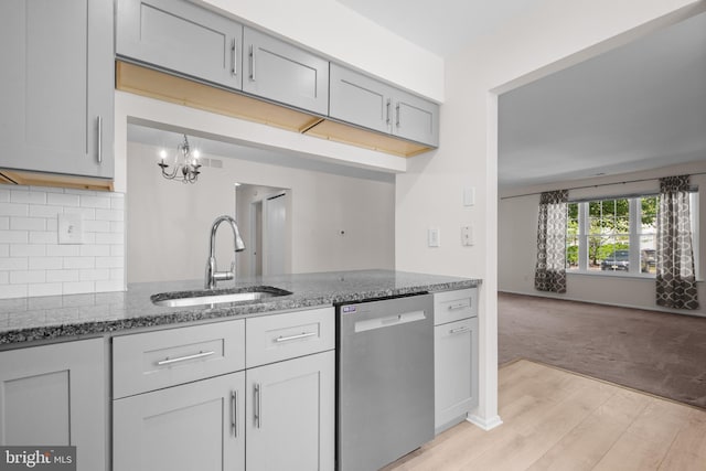 kitchen with an inviting chandelier, a sink, dishwasher, dark stone counters, and light wood-type flooring