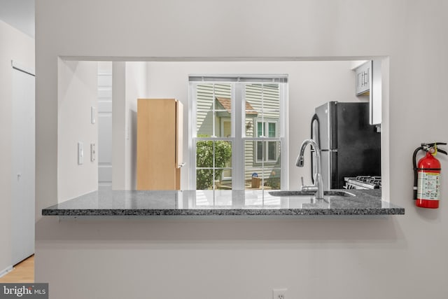 kitchen featuring a sink, dark stone countertops, freestanding refrigerator, and light wood-style flooring