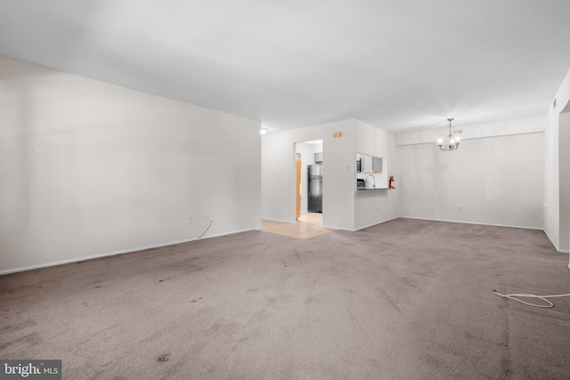 unfurnished living room with light colored carpet, baseboards, and a chandelier