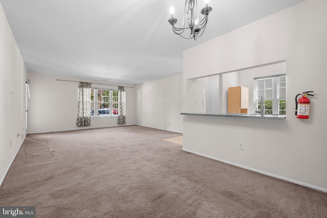 unfurnished living room featuring baseboards, carpet flooring, a sink, and a notable chandelier