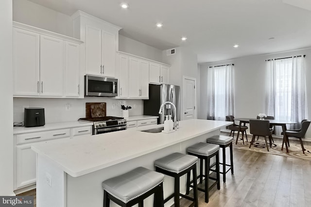 1701 Beech Leaf St, Dumfries, VA 22026 - kitchen with appliances with stainless steel finishes, a sink, an island with sink, decorative backsplash, and white cabinetry