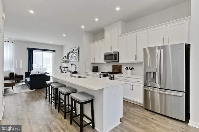 1701 Beech Leaf St, Dumfries, VA 22026 - kitchen with stainless steel appliances, a sink, white cabinetry, light wood-style floors, and a kitchen island with sink