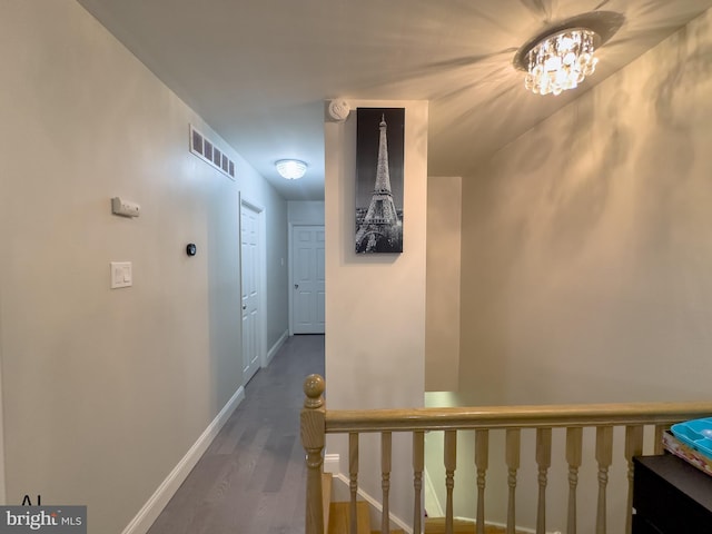 hallway featuring visible vents, wood finished floors, baseboards, a chandelier, and an upstairs landing