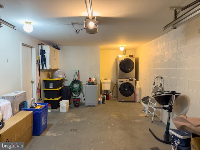 garage with concrete block wall, stacked washer / dryer, and a garage door opener