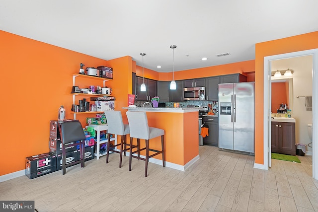 kitchen with a peninsula, stainless steel appliances, a kitchen breakfast bar, visible vents, and light wood-style flooring