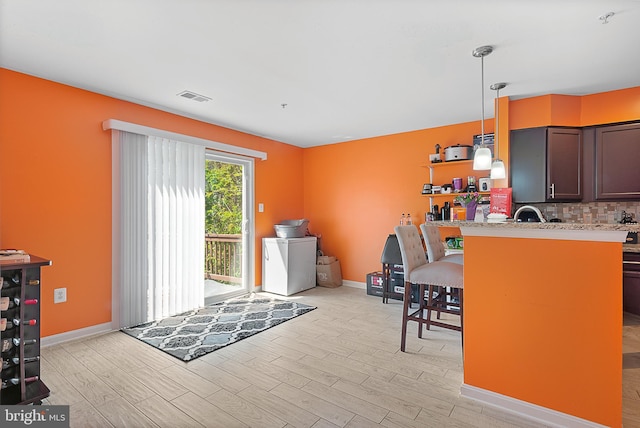 kitchen featuring a breakfast bar, visible vents, backsplash, hanging light fixtures, and light wood-style floors