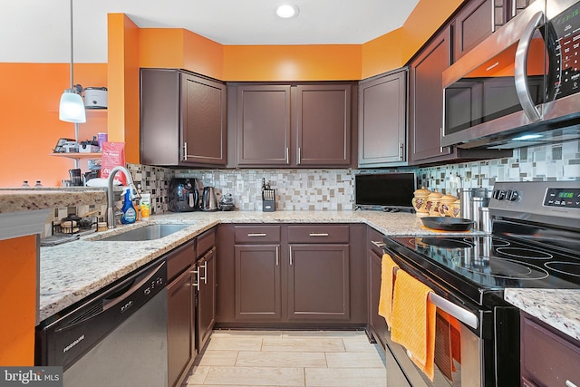 kitchen featuring a sink, stainless steel appliances, light stone counters, pendant lighting, and backsplash