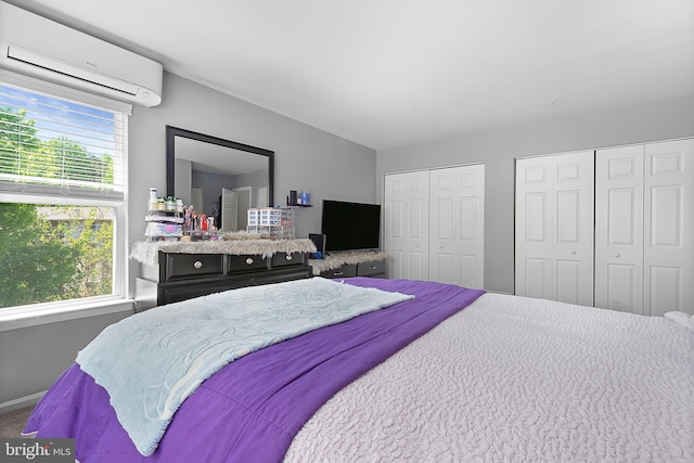 bedroom featuring multiple closets, baseboards, and a wall mounted air conditioner