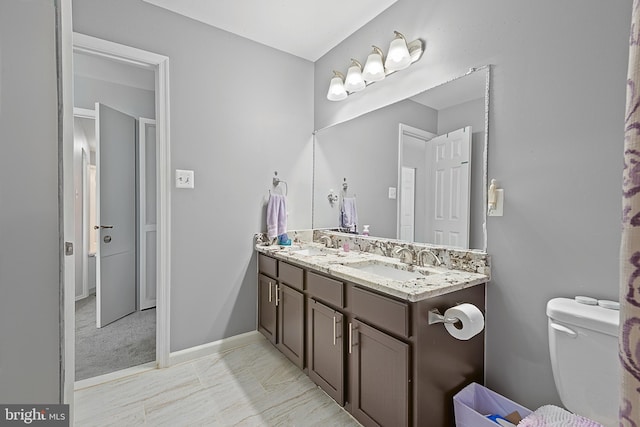 full bath with a sink, double vanity, toilet, and baseboards