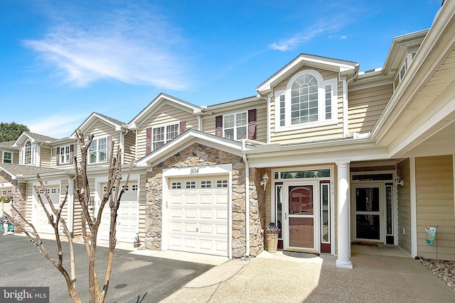 townhome / multi-family property featuring an attached garage, driveway, and stone siding