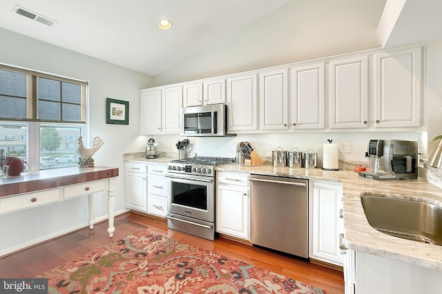 kitchen with visible vents, vaulted ceiling, light wood-style floors, stainless steel appliances, and white cabinetry