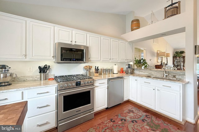 kitchen featuring white cabinets, light stone counters, a sink, stainless steel appliances, and lofted ceiling