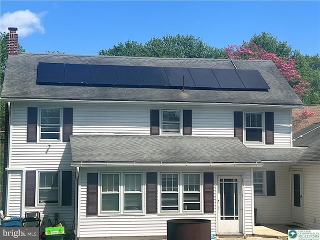 view of front of home with a chimney, a shingled roof, and solar panels