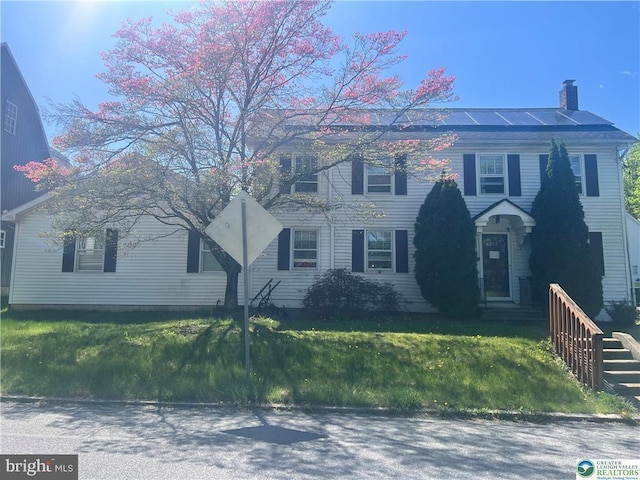 colonial inspired home with a front lawn, roof mounted solar panels, and a chimney