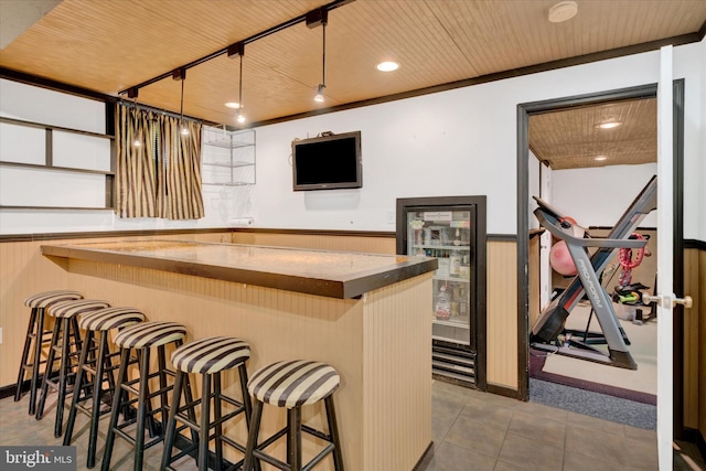 bar with tile patterned floors, wood ceiling, bar area, and beverage cooler