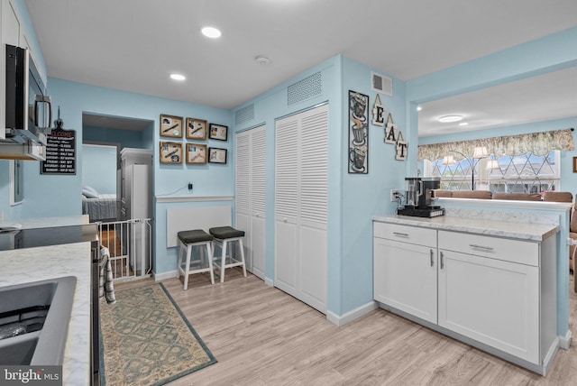 kitchen with visible vents, light wood-style flooring, stainless steel microwave, and white cabinets